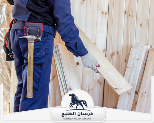 افضل نجار في الفجيرة 0547761153 فرسان الخليج نجار يحمل لوح خشب داخل الورشة استعدادًا لأعمال القص والتركيب.