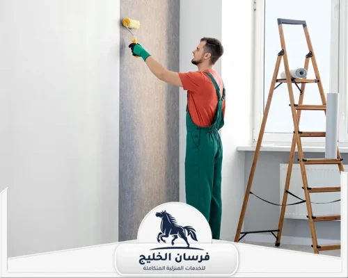 شركة صبغ في الفجيرة - فرسان الخليج صباغ يقف أمام جدار رمادي ويستخدم أسطوانة طلاء داخل غرفة مضيئة.