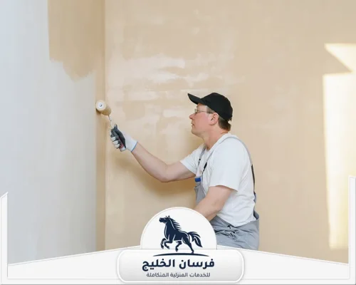 صباغ شاطر في الفجيرة - فرسان الخليج عامل صباغة يجدد جدارًا داخليًا بلون بيج فاتح مع الاهتمام بالزوايا.