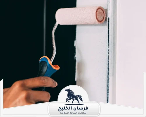 خدمات صباغ في الشارقة - فرسان الخليج عامل يمسك رول دهان أثناء تطبيق طبقة طلاء فاتحة على جدار داخلي.