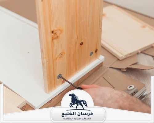 نجار تركيب غرف نوم في الفجيرة 0547761153 فرسان الخليج فني يثبت لوحًا خشبيًا بمسمار أثناء تركيب قطعة أثاث داخل المنزل.