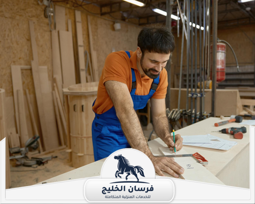 افضل نجار في دبي 0547761153 فرسان الخليج فني نجارة يراجع المخطط ويضع علامات القياس على لوح خشبي.