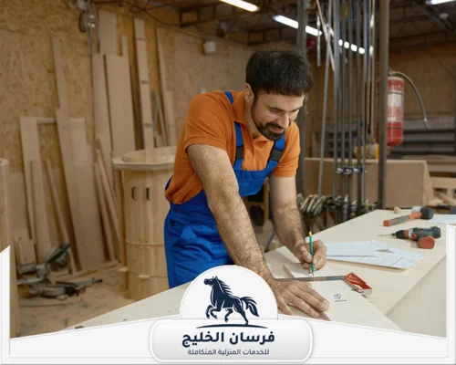 افضل نجار في دبي 0547761153 فرسان الخليج فني نجارة يراجع المخطط ويضع علامات القياس على لوح خشبي.