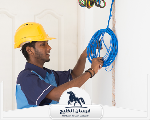 افضل كهربائي منازل في عجمان 0547761153 فرسان الخليج كهربائي منازل يرتدي خوذة أمان ويفحص أسلاك الكهرباء داخل الجدار.