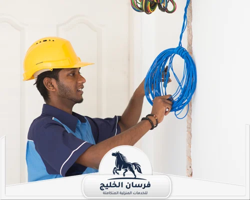 افضل كهربائي منازل في عجمان 0547761153 فرسان الخليج كهربائي منازل يرتدي خوذة أمان ويفحص أسلاك الكهرباء داخل الجدار.