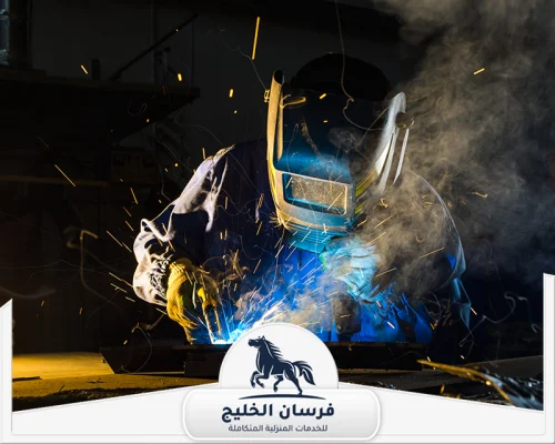 حداد هناجر في الفجيرة 0547761153 فرسان الخليج عامل حدادة يلحم قطعة معدنية مع ارتداء القناع والقفازات الواقية.