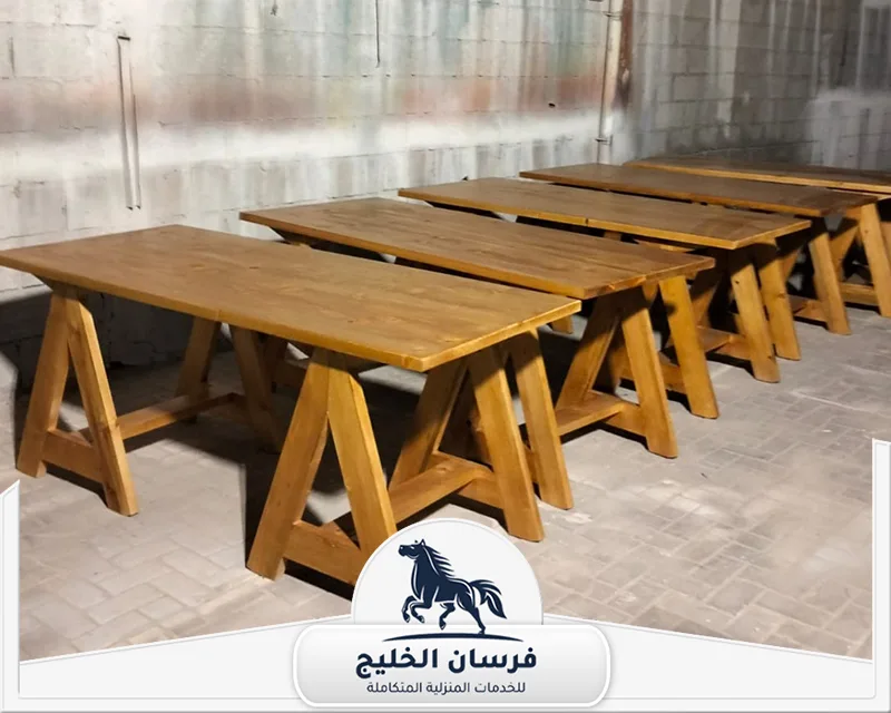 فني نجار في رأس الخيمة - فرسان الخليج مجموعة طاولات خشبية طويلة بأرجل مائلة، تعكس جودة القص والتركيب ودقة تنفيذ الأعمال الخشبية.