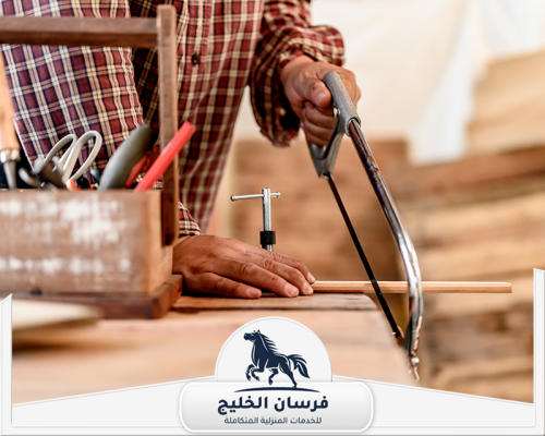 اسعار نجار في عجمان 0547761153 فرسان الخليج نجار يستخدم منشارًا يدويًا لقص قطعة خشب داخل ورشة العمل.