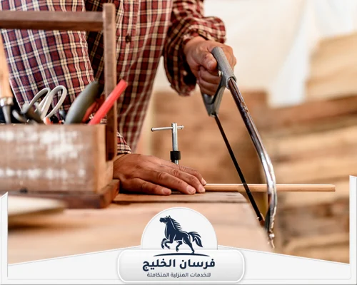 اسعار نجار في عجمان 0547761153 فرسان الخليج نجار يستخدم منشارًا يدويًا لقص قطعة خشب داخل ورشة العمل.