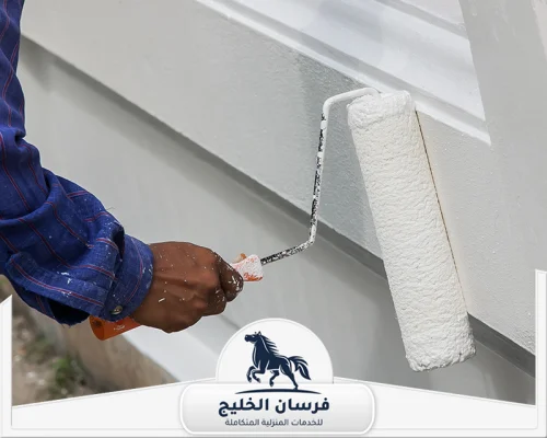 صباغ ديكور في عجمان - فرسان الخليج عامل دهانات يطلي واجهة خارجية باللون الأبيض باستخدام رول الطلاء.