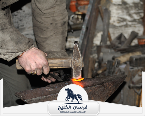 فني حدادة يستخدم المطرقة لتشكيل حلقة معدنية متوهجة فوق السندان.