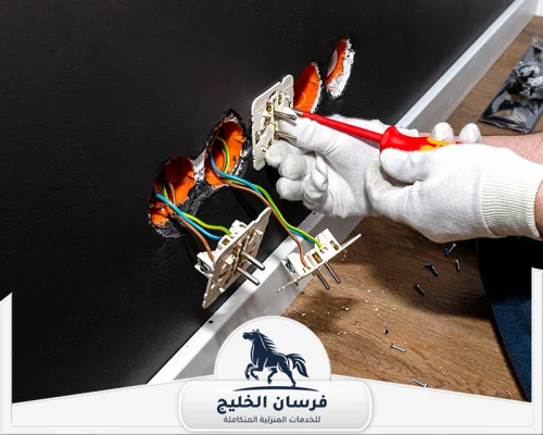 مميزات كهربائي منازل في الشارقة 0547761153 فرسان الخليج كهربائي يصلح عدة مقابس كهرباء داخل جدار أسود باستخدام مفك معزول.