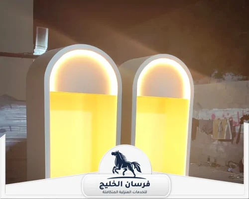 نجار اثاث منزلي في أم القيوين - فرسان الخليج قطعتا ديكور خشبيتان بتصميم مقوس وإضاءة صفراء مدمجة.