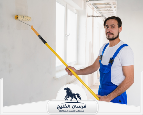 شركة صباغة في أم القيوين 0547761153 فرسان الخليج عامل صباغة ينفذ طلاء الحائط الأبيض بالقرب من النافذة.