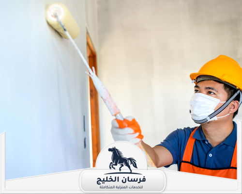 معلم دهانات في عجمان 0547761153 فرسان الخليج فني دهانات يطلي الجدار بالرول مع ارتداء خوذة وكمامة وقفازات واقية.