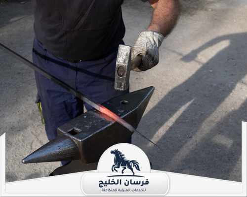 حداد شبابيك في دبي 0547761153 فرسان الخليج حداد يطرق قضيبًا حديديًا ساخنًا فوق السندان لتشكيله بدقة.