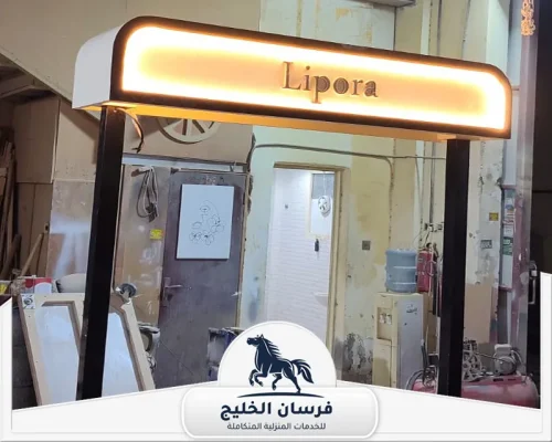 نجار خشب في دبي - فرسان الخليج لافتة مضيئة باسم Lipora داخل ورشة، بإطار أسود وتصميم مستطيل بحواف دائرية.