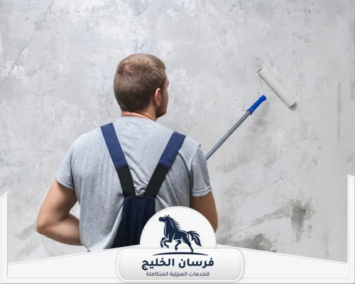 صباغ بدبي 0547761153 فرسان الخليج فني دهانات يطبق طبقة طلاء على جدار رمادي داخل المنزل.