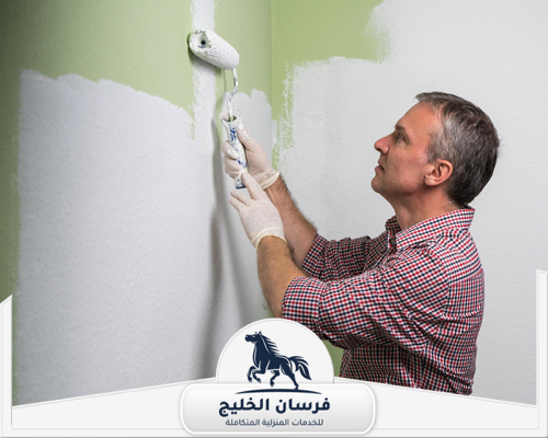صباغ ممتاز في دبي 0547761153 فرسان الخليج فني دهانات يوزع الطلاء الأخضر على الحائط بطريقة منتظمة.