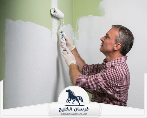 صباغ ممتاز في دبي 0547761153 فرسان الخليج فني دهانات يوزع الطلاء الأخضر على الحائط بطريقة منتظمة.