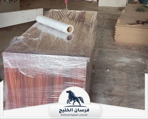 نجار خشب الشارقة - فرسان الخليج قطعة أثاث خشبية كبيرة مغلفة بالبلاستيك داخل ورشة نجارة.