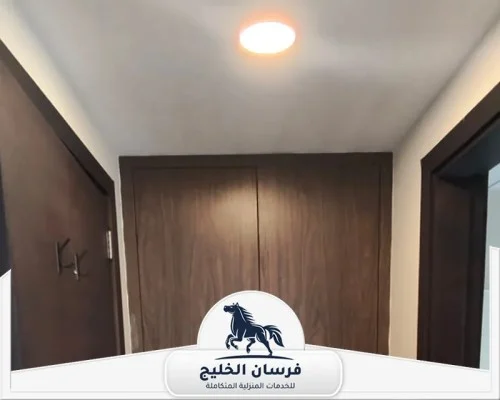 نجار في السيوح بالشارقة - فرسان الخليج أبواب وخزانة خشبية بتصميم موحد داخل ممر منزلي حديث مع إضاءة دائرية في السقف.